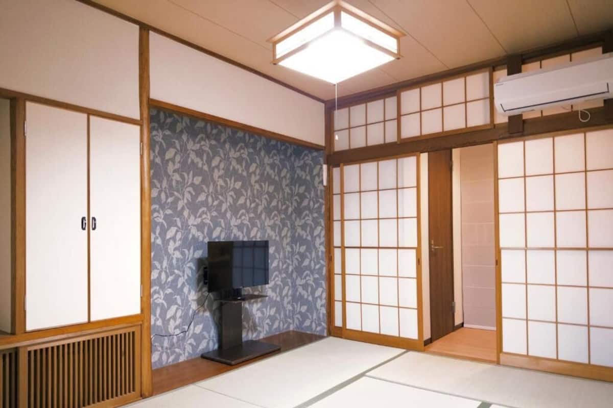 Ein traditioneller japanischer Raum mit Tatami-Böden, Schiebetüren, einem Fernseher und einem Deckenventilator.