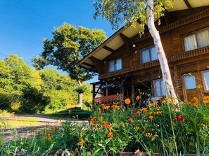 A wooden building with a balcony and a garden with orange flowers. - Yado Brodiaea (Myoko)