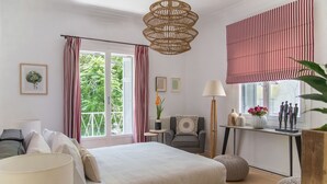 Un dormitorio con cama, mesitas de noche, una silla, un escritorio y una ventana con cortinas.