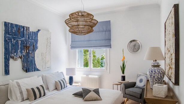 Un dormitorio con cama, una silla, un ventanal con vistas, una lámpara colgante y una pared decorada con obras de arte.