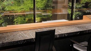 A modern kitchen with a large window overlooking a garden, featuring a marble countertop and two black chairs. - Sushi Auberge Gorasaryo (Hakone)