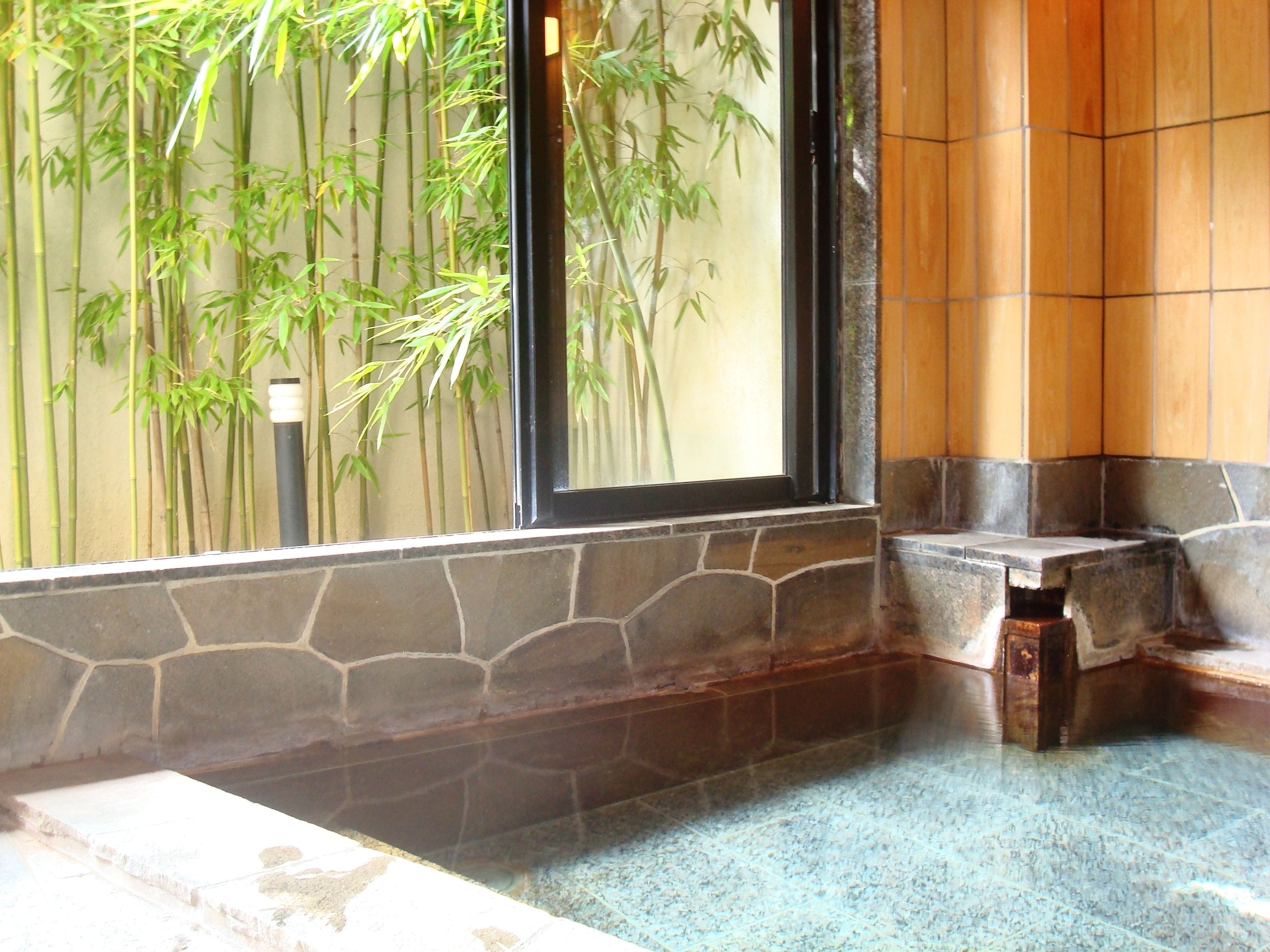 A stone-tiled bathroom with a bamboo plant outside a window.