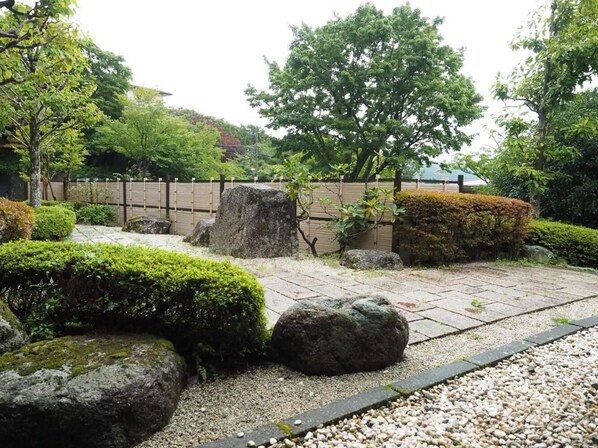 Un jardín japonés tradicional con faroles de piedra, una cerca de madera y abundante vegetación.