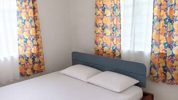 Habitación de hotel con cama, unidad de aire acondicionado, cortinas con motivos florales y piso de baldosas.