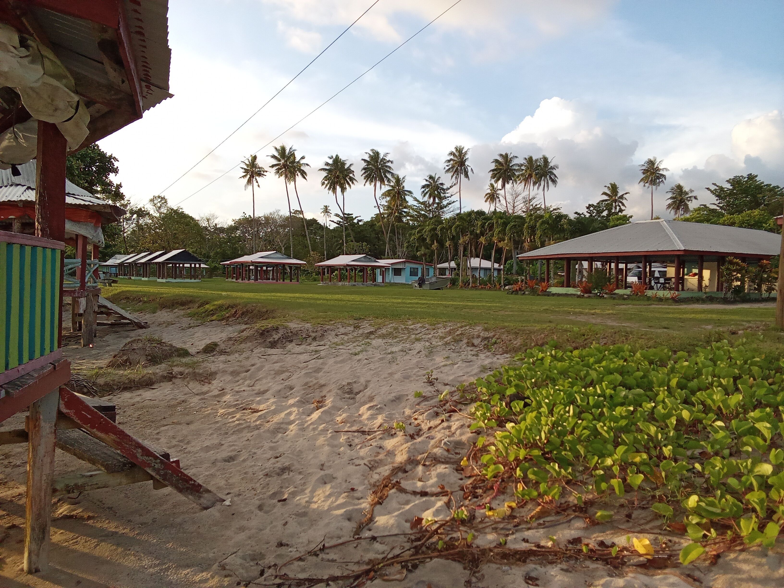 Ein Strandresort mit mehreren bungalowsähnlichen Gebäuden, einem Sandstrand und Palmen im Hintergrund.