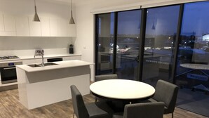 Een moderne keuken met een centraal eiland, een eetgedeelte met een ronde tafel en stoelen, en grote ramen met uitzicht op de stadslijn.