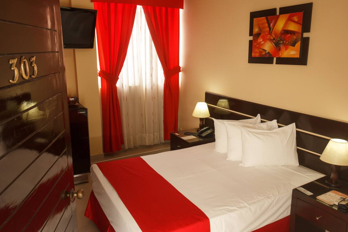 A hotel room with a bed, two bedside tables, a TV, and a door with the number 303.