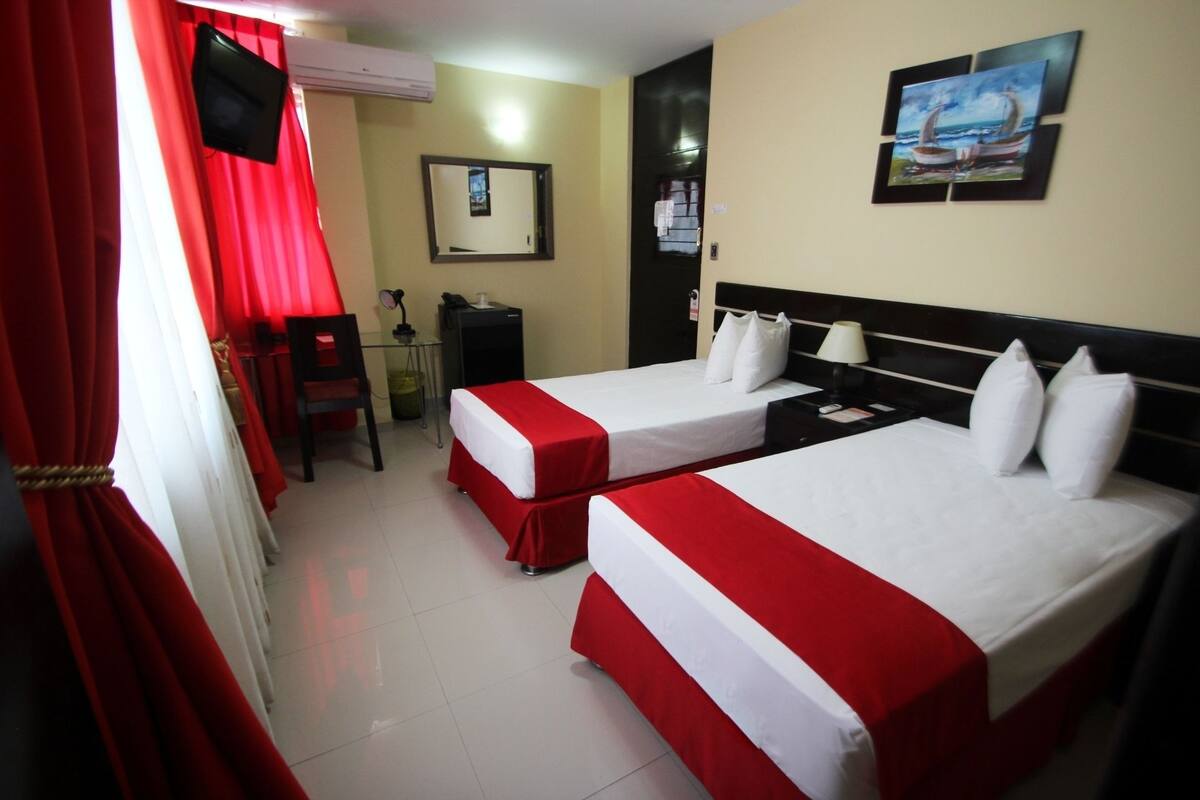 A hotel room with two beds, a desk, a chair, a TV, and a painting on the wall.
