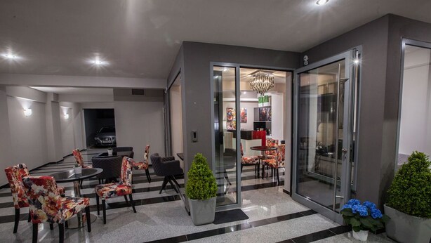 A modern lobby with a checkered floor, seating area with floral chairs, and a glass door leading to a room with a chandelier. - Diamond city living (Drama)