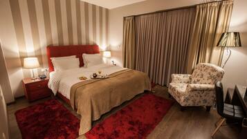 A hotel room with a bed, a nightstand, a chair, a red rug, and curtains.