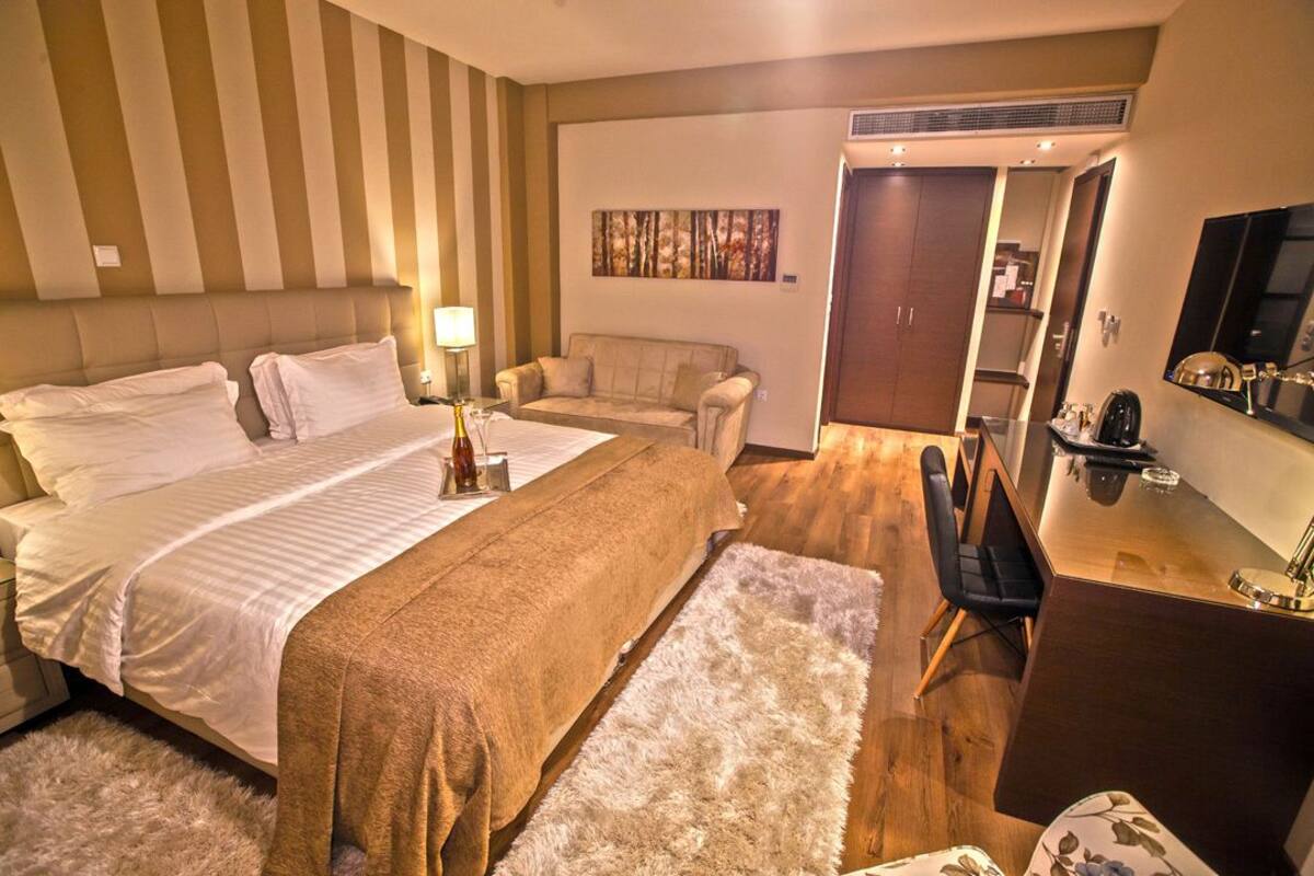 Une chambre d’hôtel avec un grand lit, un bureau, une chaise, un canapé et une armoire.