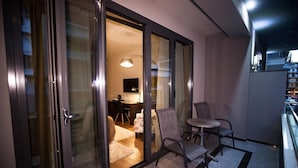 A balcony with a glass door leading to a room, a small table with chairs, and a rug on the floor. - Diamond city living (Drama)