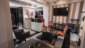 A modern hotel lobby with a seating area, a flat-screen TV, and a staircase leading to the upper floors. - Diamond city living (Drama)