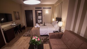 A hotel room with a bed, a sofa, a TV, a desk, and a coffee table with flowers. - Diamond city living (Drama)