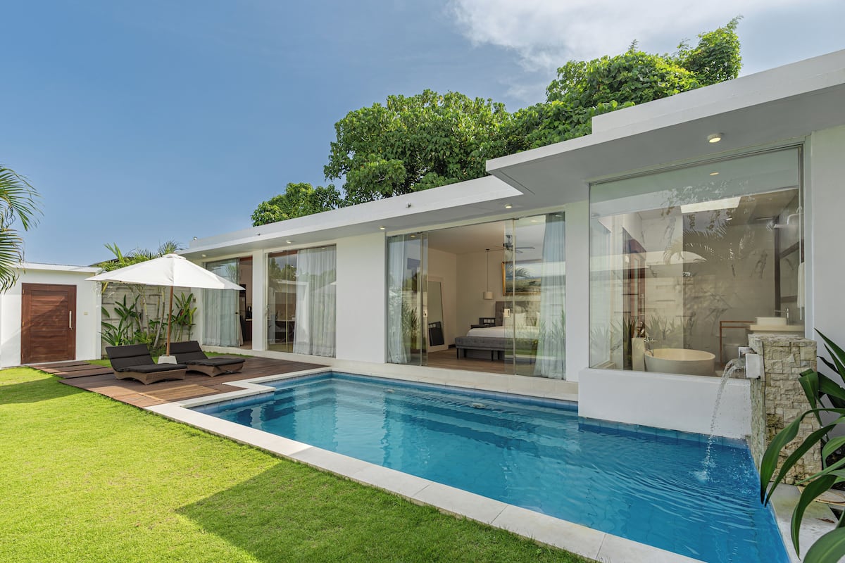 A modern house with a swimming pool, a patio with lounge chairs, and a large glass door leading to a living area.