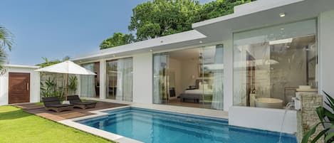 A modern house with a swimming pool, a patio with lounge chairs, and a large glass door leading to a living area.