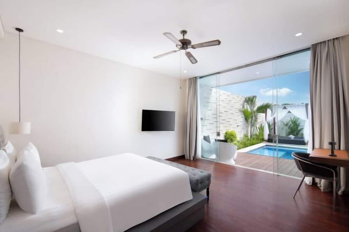 A modern hotel room with a bed, a desk, a chair, a TV, and a view of a swimming pool.