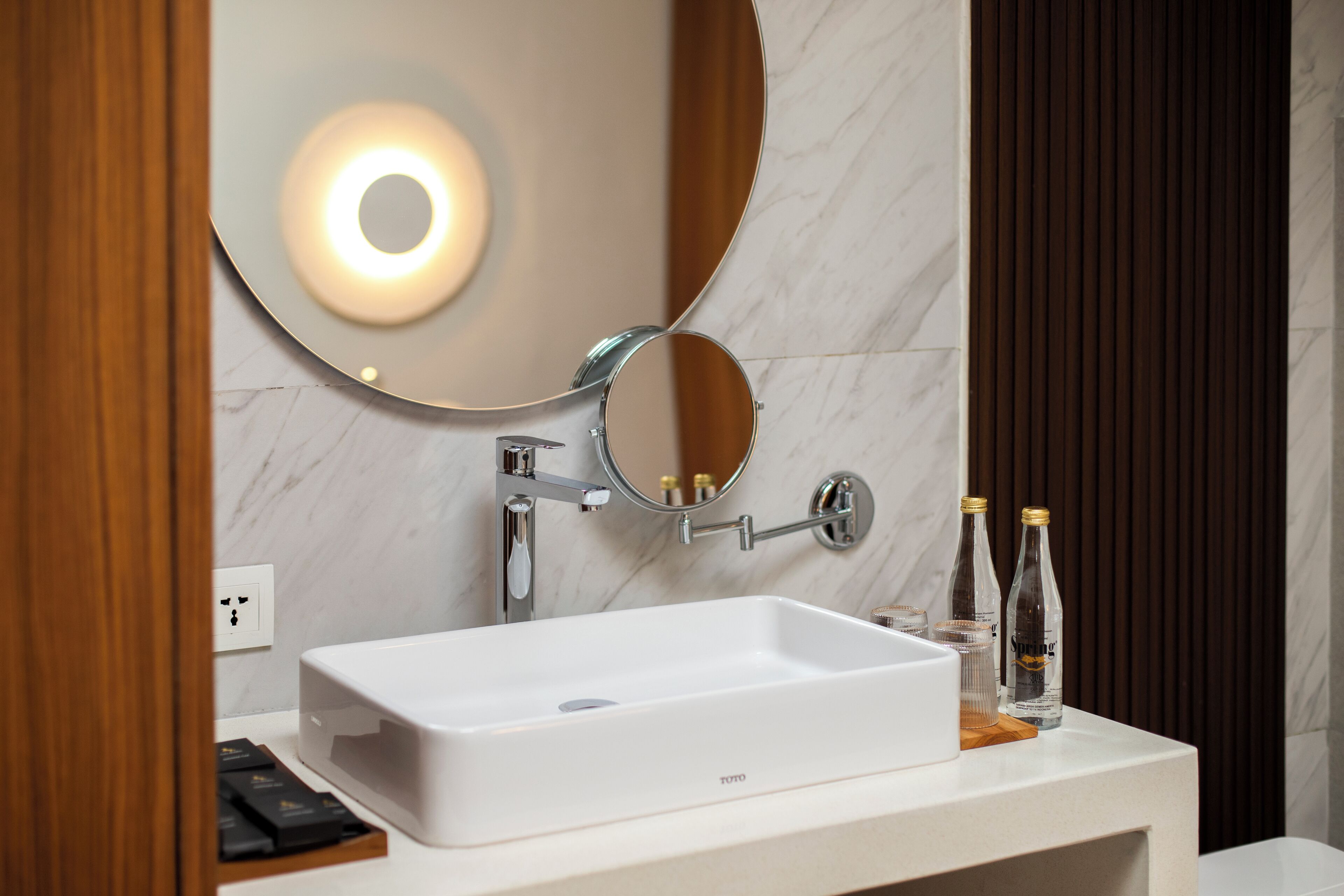 A modern bathroom with a white sink, a round mirror, and two bottles of hand sanitizer on the counter.