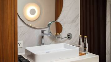 A modern bathroom with a white sink, a round mirror, and two bottles of hand sanitizer on the counter.