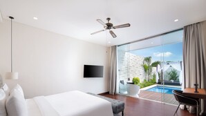 Quarto de hotel moderno com uma cama grande, TV de tela plana, ventoinha no teto e vista para uma piscina e área externa.