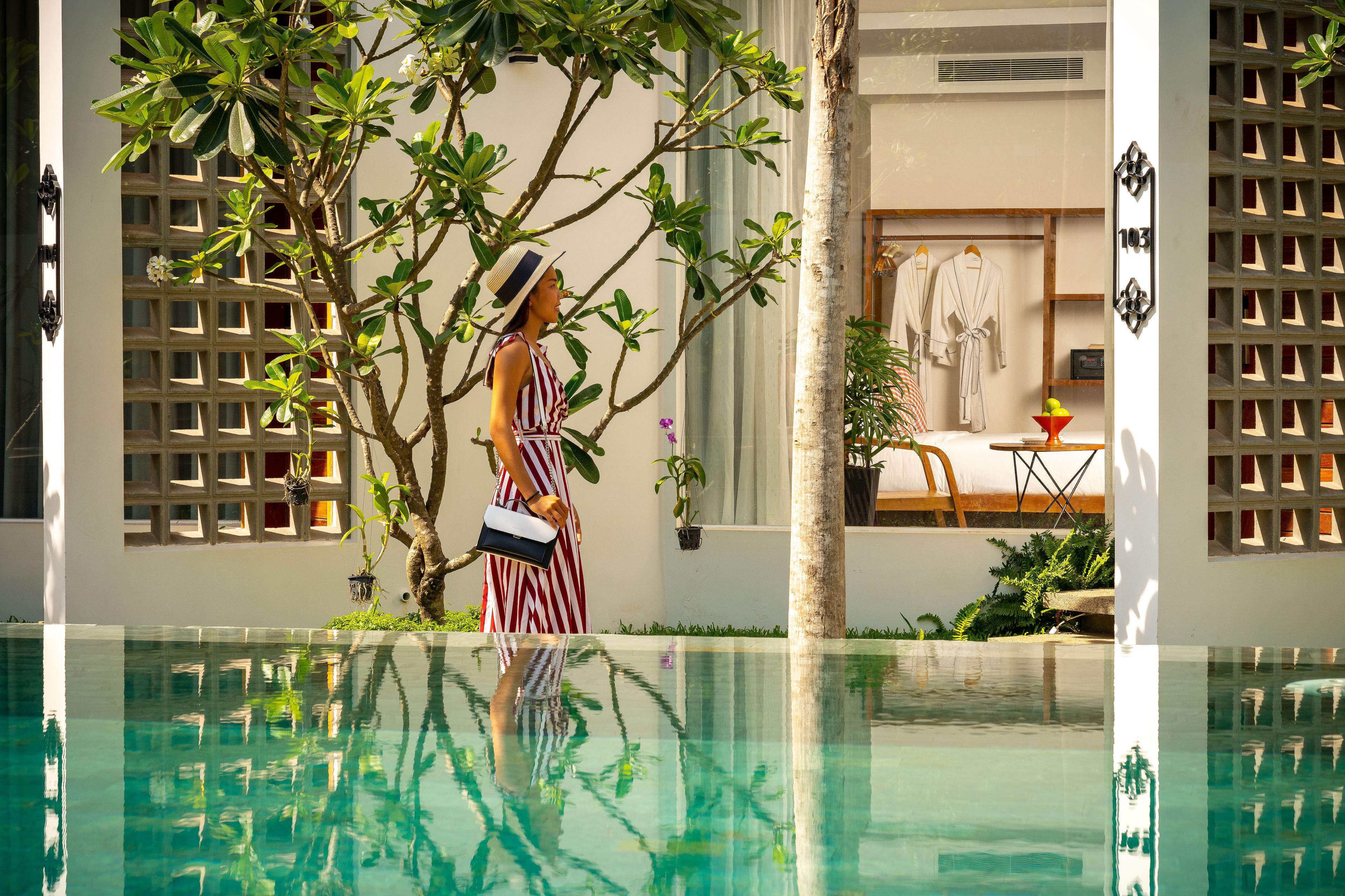 A woman standing by a pool with a tree and a building in the background.