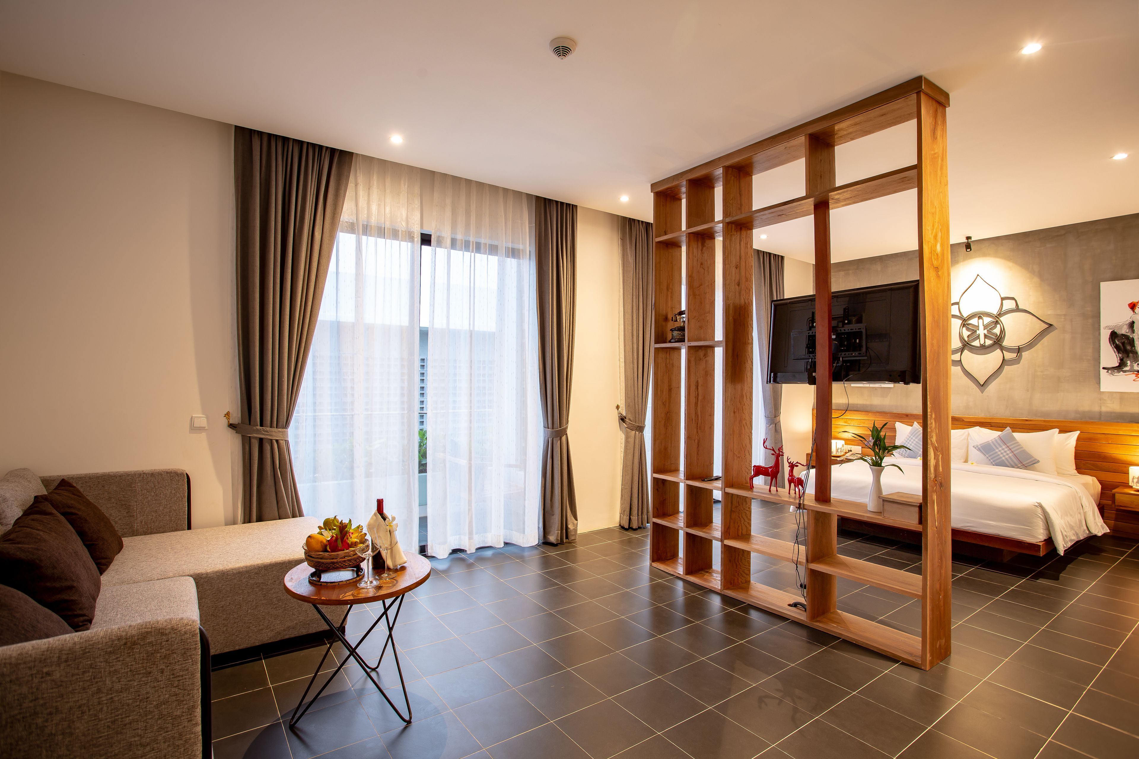 Habitación de hotel moderna con sofá, una mesita con frutero, cama con cabecera de madera y un ventanal con cortinas.