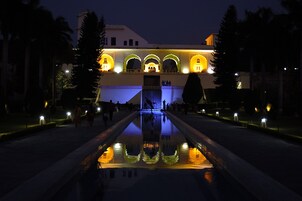 Vista nocturna de un edificio con arcos iluminados y una fuente central que refleja las luces.