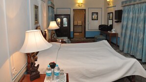 A hotel room with a bed, two bedside lamps, a nightstand with a lamp, a chair, a desk with a computer, a television, and a door leading to another room. - The Fort Nalagarh (Nalagarh)