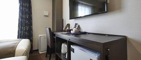 A hotel room with a bed, a desk with a television, a coffee maker, and a mini-fridge.