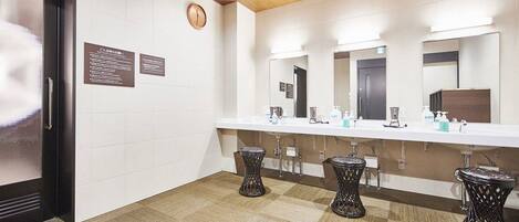 Une salle de bain moderne avec un mur recouvert de carreaux blancs, un plafond en bois et un long comptoir doté d’éviers et de tabourets.