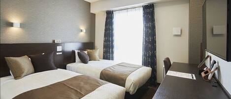 A hotel room with two beds, a desk, and a large window with curtains.