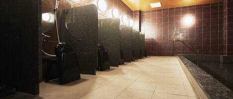 A row of public restrooms with individual stalls, a tiled floor, and a wooden ceiling.