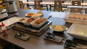 A buffet table with various dishes, including pasta, vegetables, and bread, in a restaurant setting.
