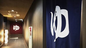 A hallway with a prominent logo on the wall, a red banner with a white emblem, and a sign with a red circle and white cross.