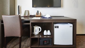 Une chambre d’hôtel équipée d’un bureau, d’une chaise, d’une télévision, d’une machine à café, d’un mini-réfrigérateur et d’un panneau de commande.