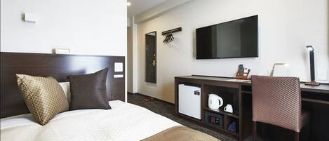 Habitación de hotel con cama, escritorio, televisor de pantalla plana, mini refrigerador, cafetera y una silla.
