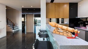 A modern kitchen with a wooden sushi rolling tool on the counter, a bar area with stools, and a staircase leading to another room. - Jia Xiang Lin Guan Hai Homestay 2 (Magong)