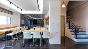 A modern dining area with a long table and chairs, a marble backsplash, and a staircase leading to an upper level. - Jia Xiang Lin Guan Hai Homestay 2 (Magong)
