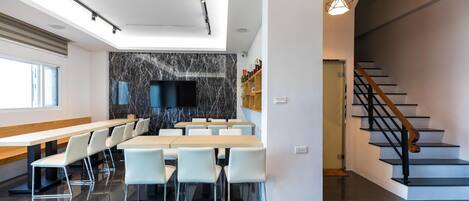 Un comedor moderno con una larga mesa y sillas, un protector de salpicaduras de mármol y una escalera que sube a un nivel superior.