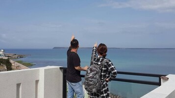 Dos personas en un balcón con vista al mar y cielo despejado.