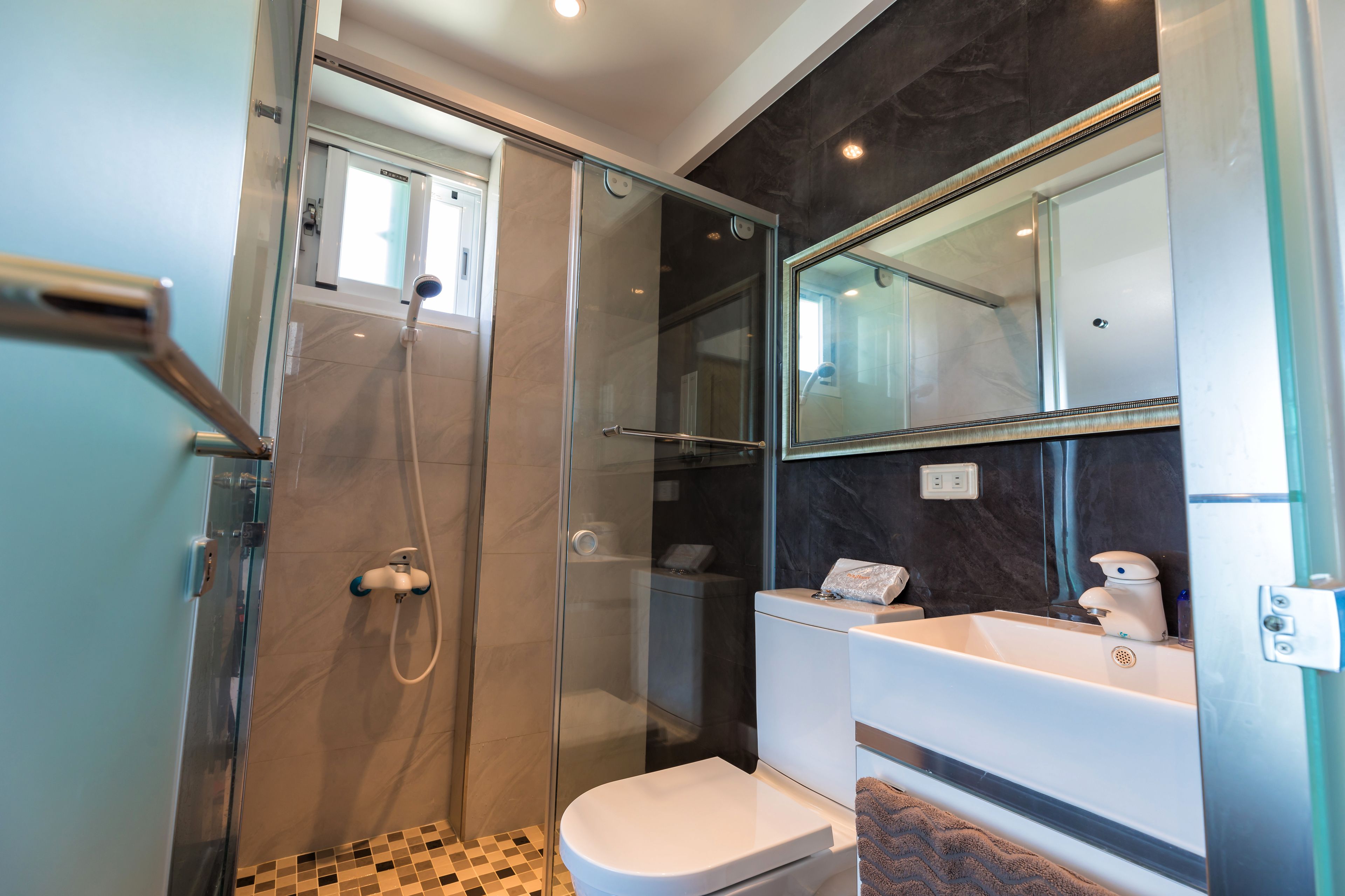 A modern bathroom with a glass-enclosed shower, a white toilet, and a sink with a mirror above it.