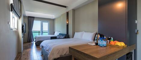Habitación de hotel con suelo de madera, una cama, un escritorio con lámpara y vistas al mar a través de una ventana.