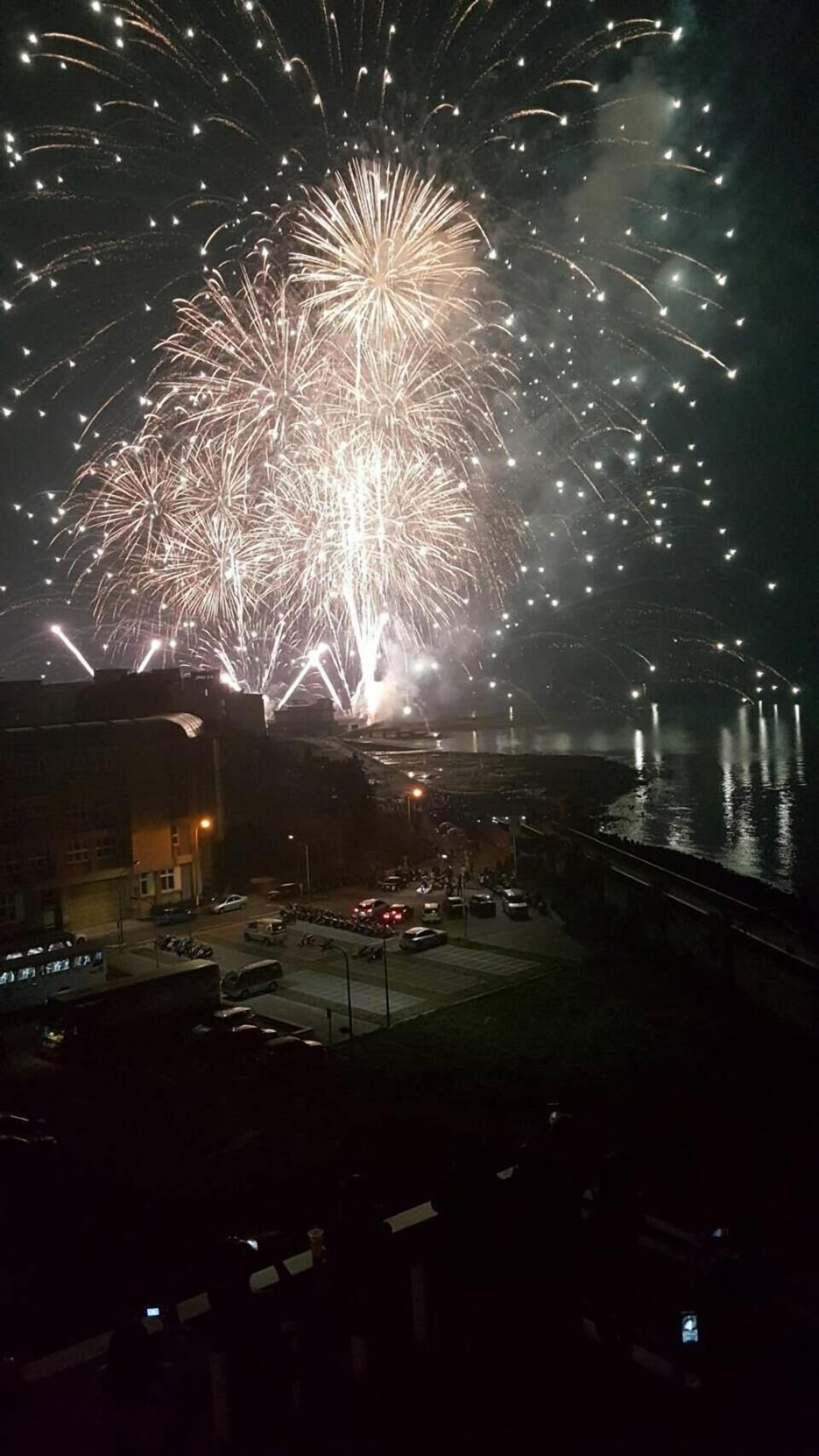 A fireworks display over a waterfront area with a bridge in the background.