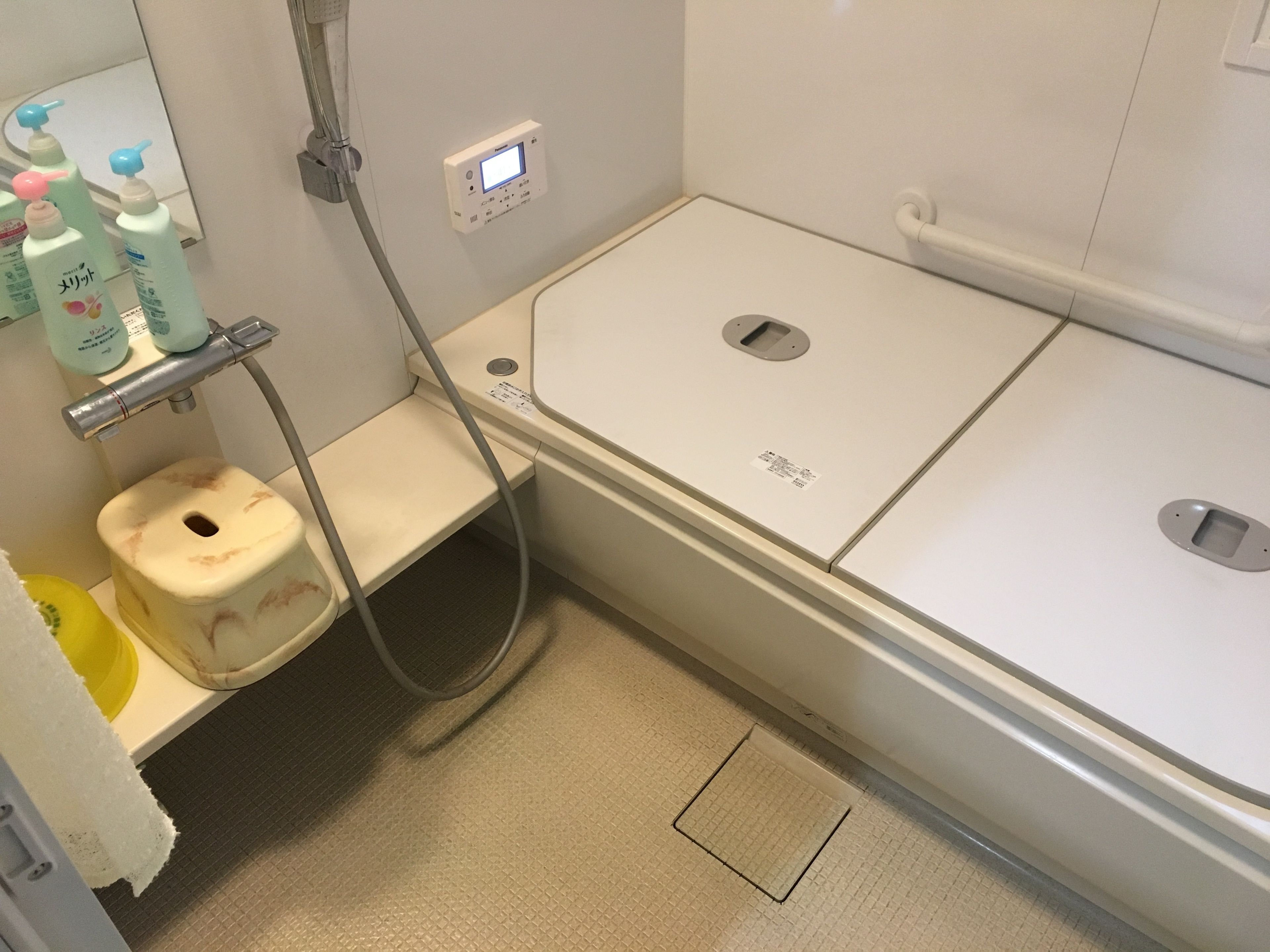 A small, private bathroom with a toilet, a shower, and a sink. There are toiletries on the wall and a toilet paper holder.