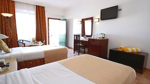 Quarto de hotel com duas camas, uma mesa de trabalho com cadeira, televisão e janela com cortinas.
