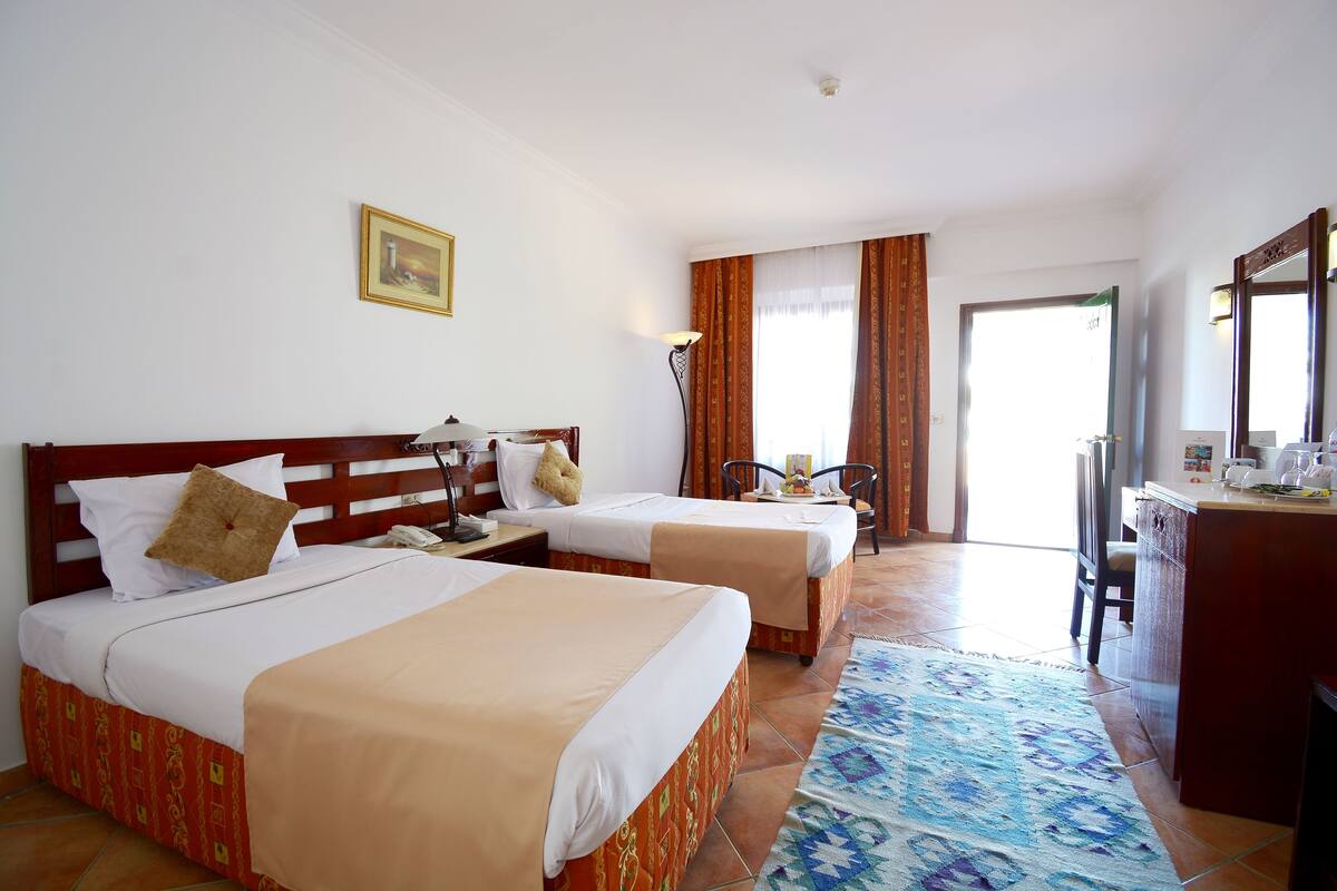 Une chambre d’hôtel avec deux lits, un bureau, une chaise et une grande fenêtre avec des rideaux.