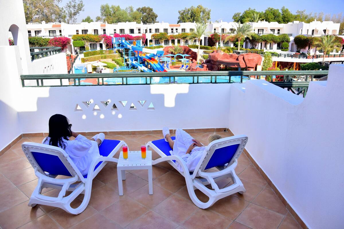 Un balcon avec deux fauteuils et une table, donnant sur un espace piscine agrémenté d’un toboggan et de formations rocheuses.