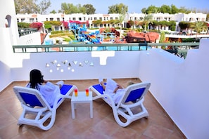 A balcony with two lounge chairs and a table, overlooking a pool area with a water slide and rock formations. - Verginia Sharm Resort & Aqua Park (Sharm El Sheikh)