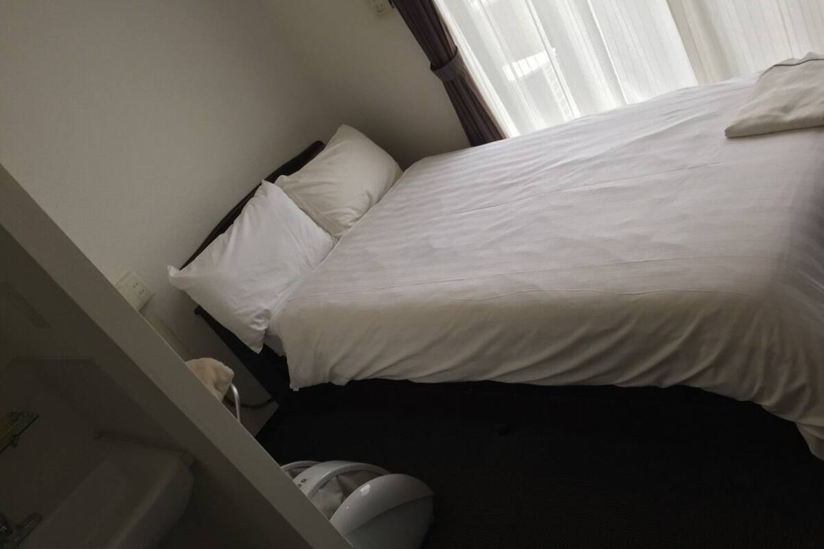 Habitación de hotel con cama, almohada, mesita de noche y zona de baño que incluye lavabo e inodoro.