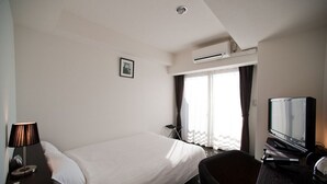 Una habitación de hotel con cama, escritorio con lámpara, televisor y aire acondicionado.
